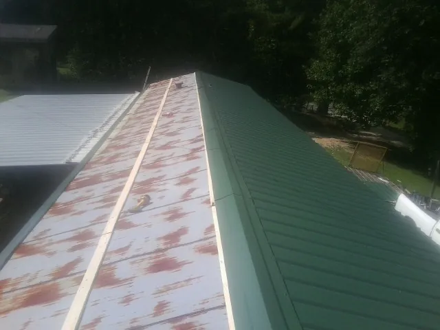 Old rusted panels beside newly installed green metal roofing — Wind Damage Roof Repair by Roofing Brothers in Dutton