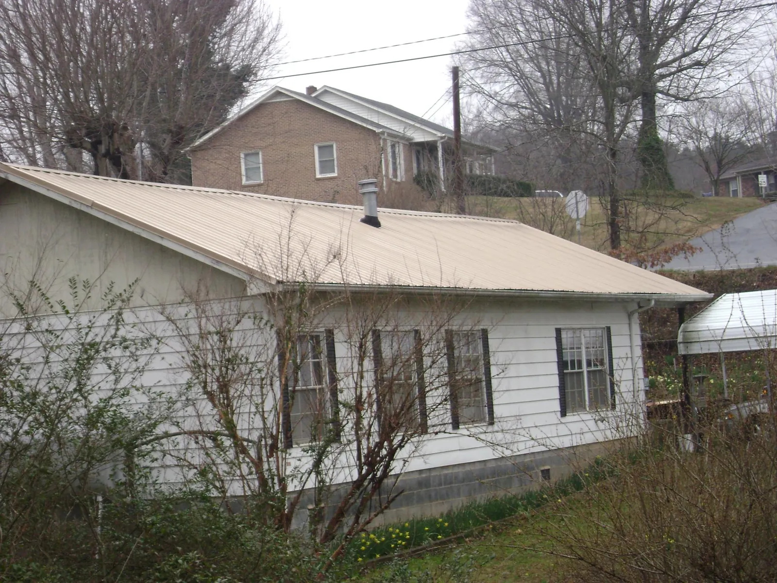 Tan metal roof on a white sided house set into a hillside — Commercial Roofing by Roofing Brothers in Dutton