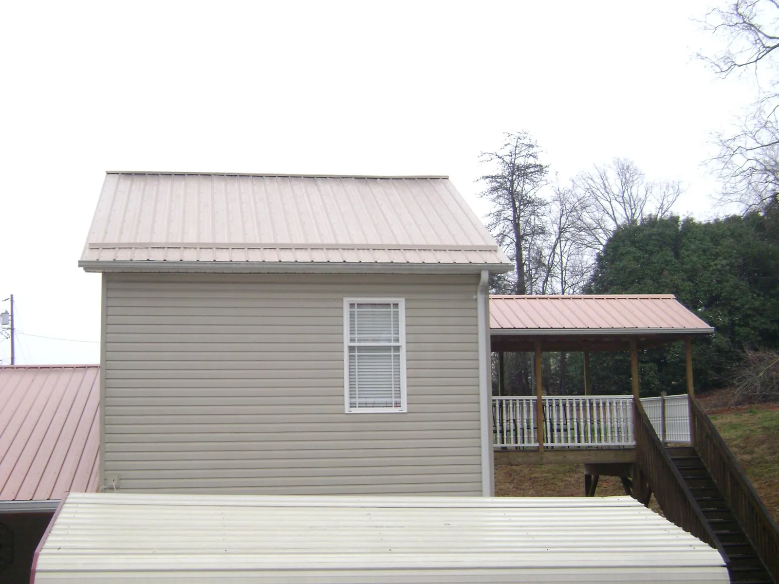Tan metal roofs on a two story addition and attached porch, from a Roof Replacement job in Dutton